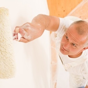 Maler streicht mit Farbrolle eine weiße Wand, Renovierung und Innenanstrich im Haus.