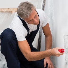 Maler streicht mit Farbrolle eine weiße Wand, Renovierung und Innenausbau im Haus.
