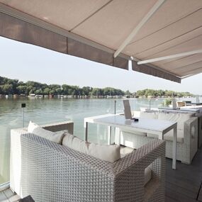 Moderne Terrasse mit weißen Loungemöbeln und Blick aufs Wasser in idyllischer Natur.
